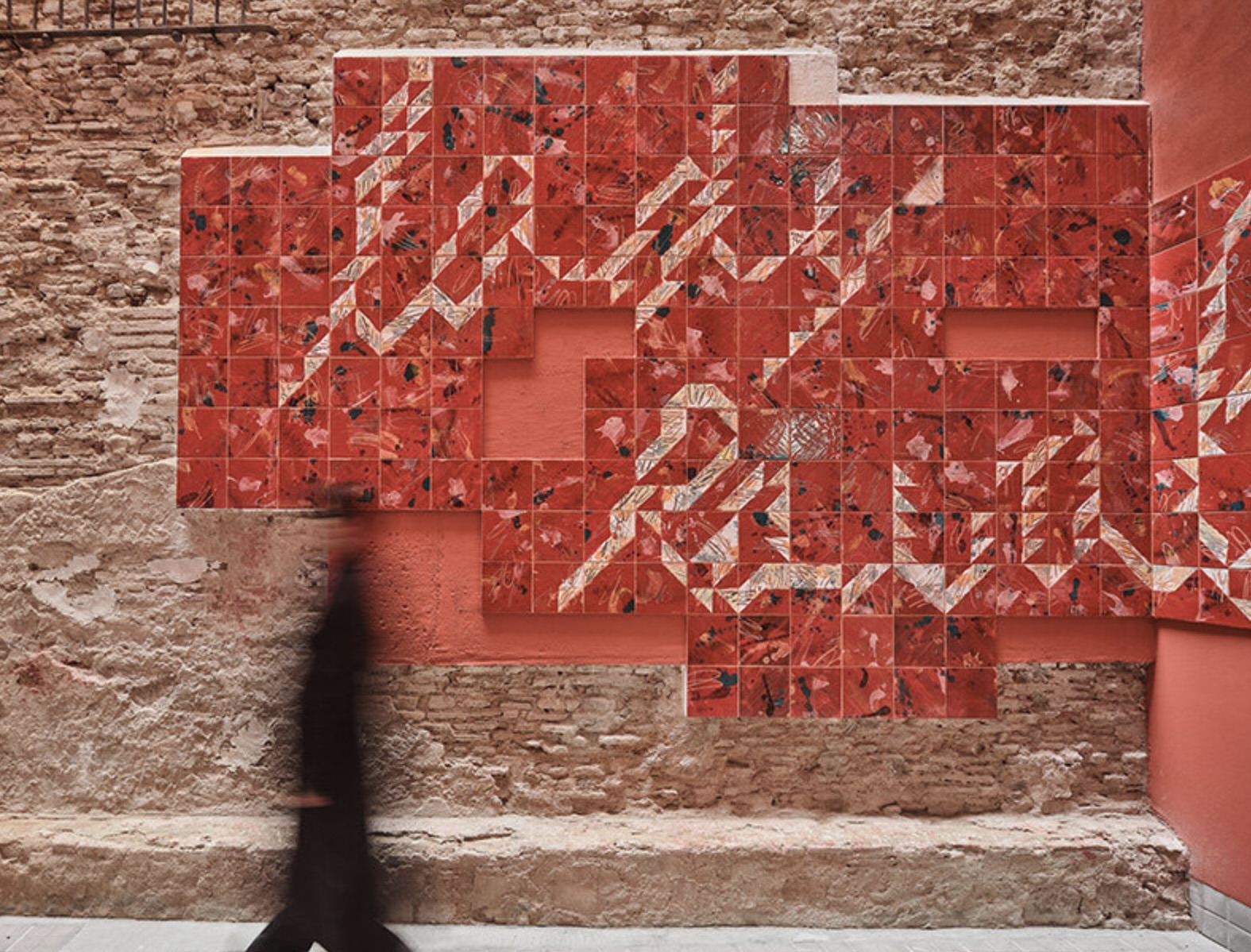 A ceramic tile mural in red tones on a courtyard wall in Barcelona’s Raval, part of the Lady Raval social housing project